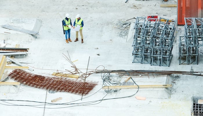 2 builders viewing blueprint plan on a construction site.