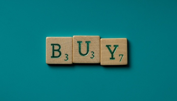 three scrabble pieces spelling the word buy on a green background