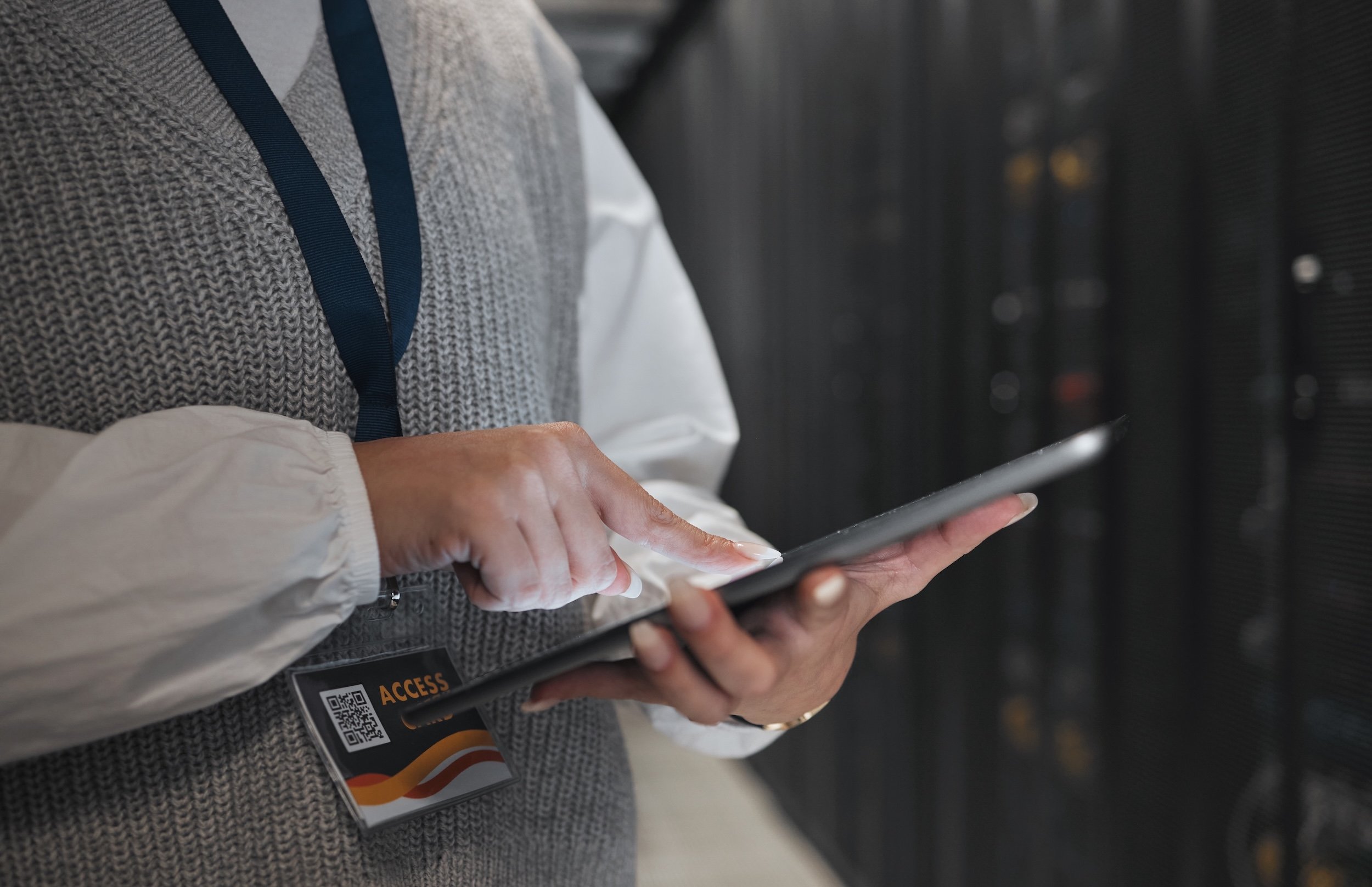 A business professional using a tablet in a data centre environment, wearing an access badge, representing operational control in a technology setting.