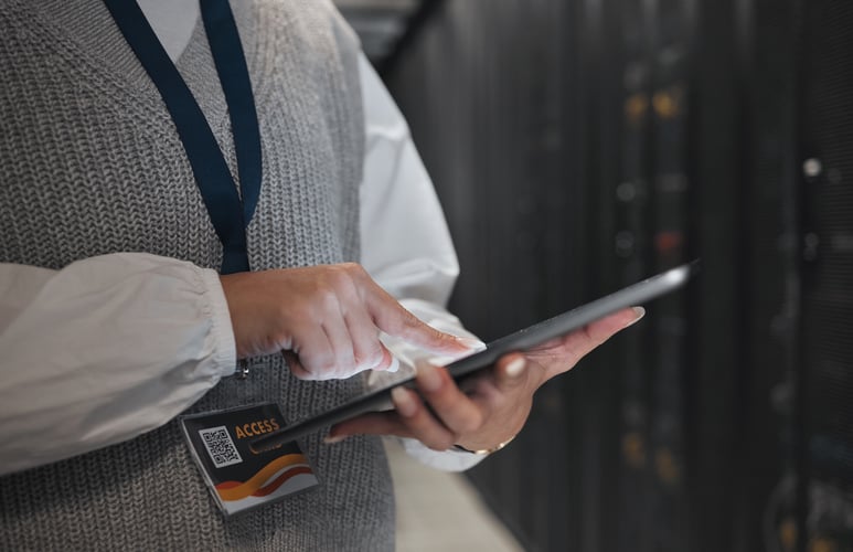 A business professional using a tablet in a data centre environment, wearing an access badge, representing operational control in a technology setting.